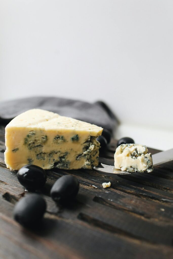 A delectable piece of blue cheese on a wooden board, garnished with black olives, perfect for gourmet presentations.