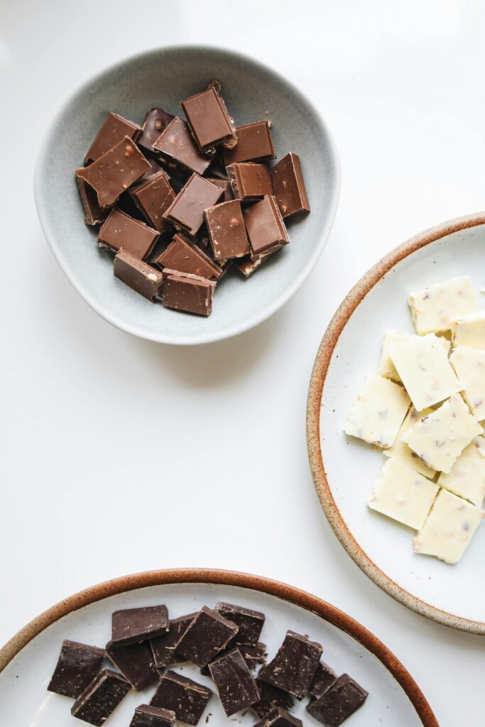 Top view of assorted milk, white, and dark chocolate pieces in ceramic bowls. Perfect for sweet indulgence.